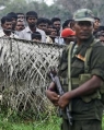 Sri Lankan Army soldier stands guard next to a fence, as internally displaced civilians look on in the background at a camp in Vavuniya, Sri Lanka